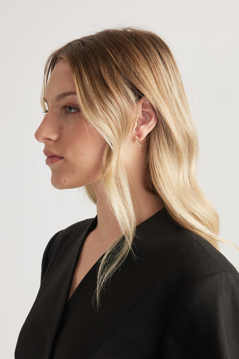 Side profile of a woman wearing a small textured gold hoop earring