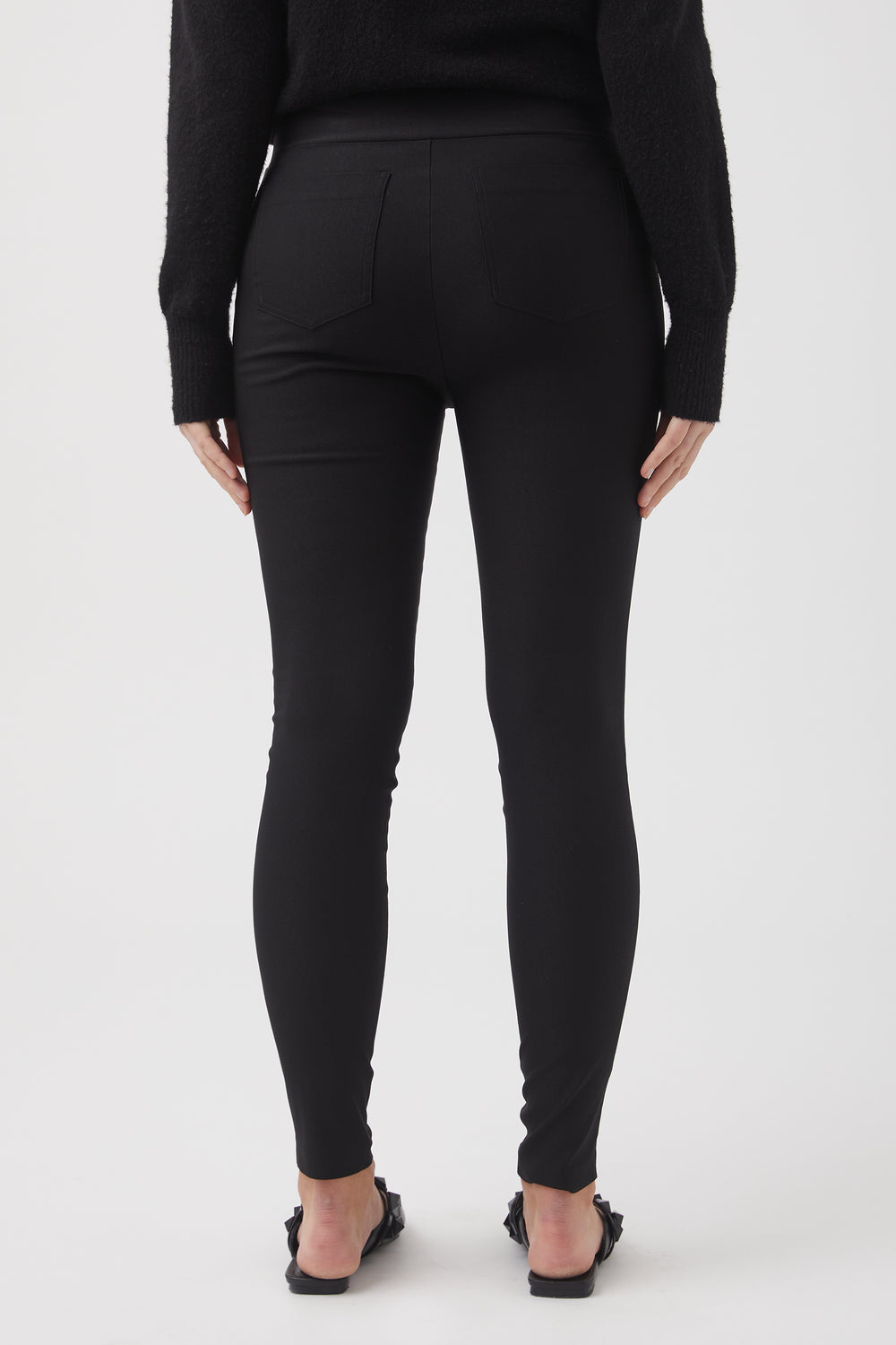 Back view of woman wearing fitted black bengaline pants paired with a black sweater and sandals