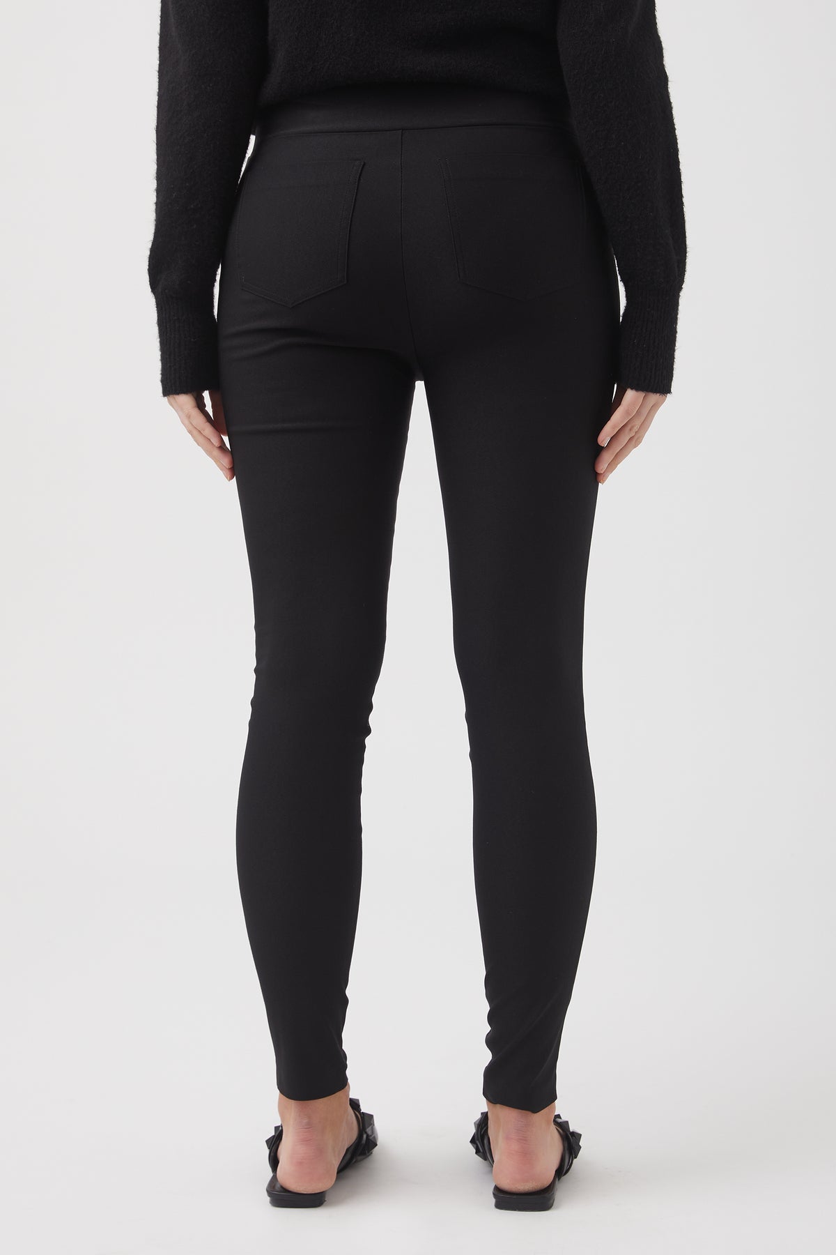Back view of woman wearing fitted black bengaline pants paired with a black sweater and sandals