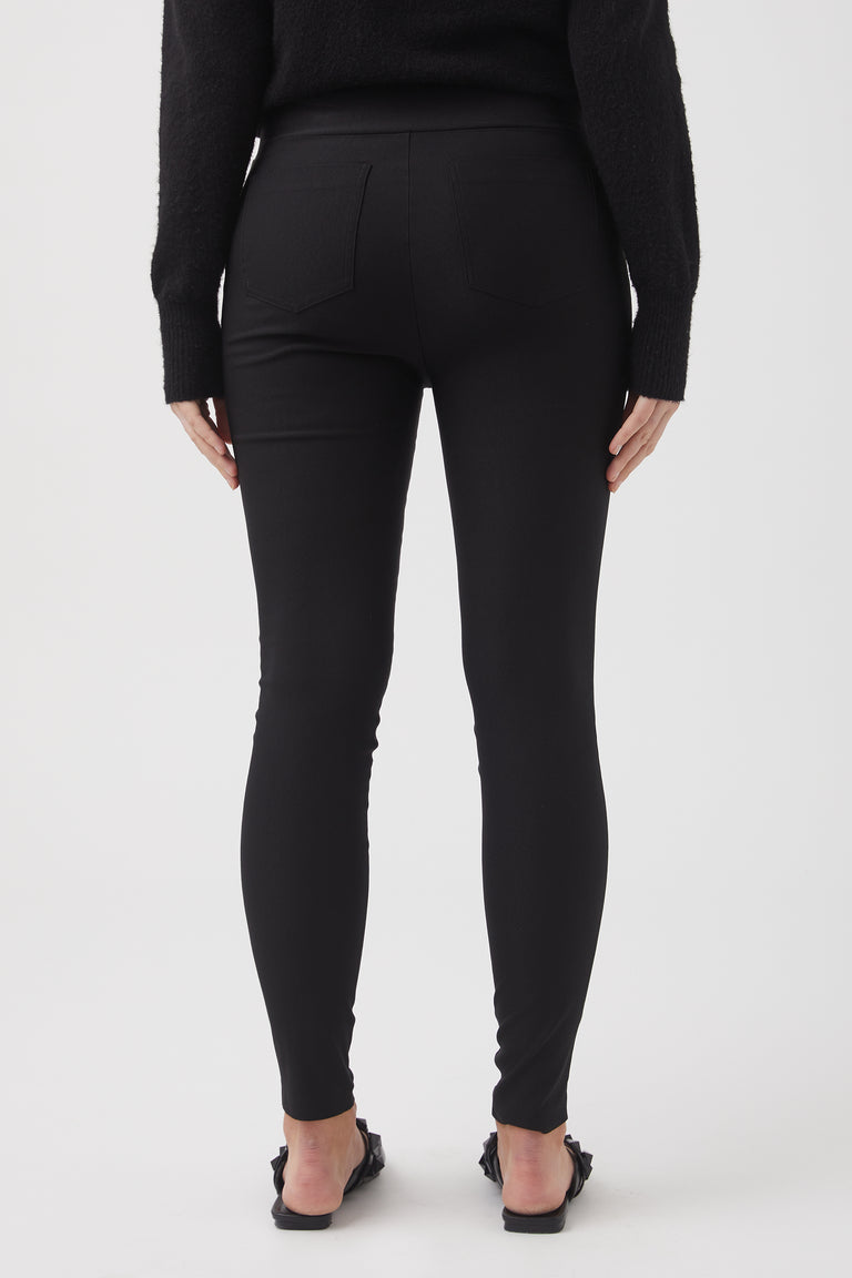 Back view of woman wearing fitted black bengaline pants paired with a black sweater and sandals