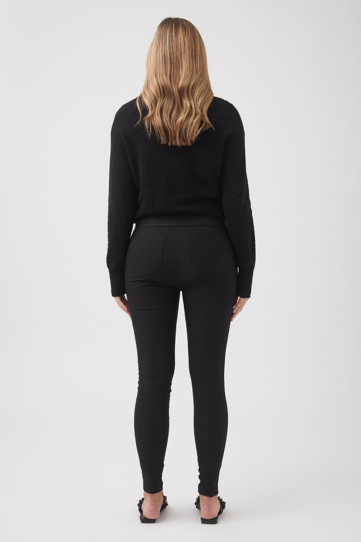 Woman wearing fitted black bengaline pants and a textured black sweater, shown from behind with loose hair