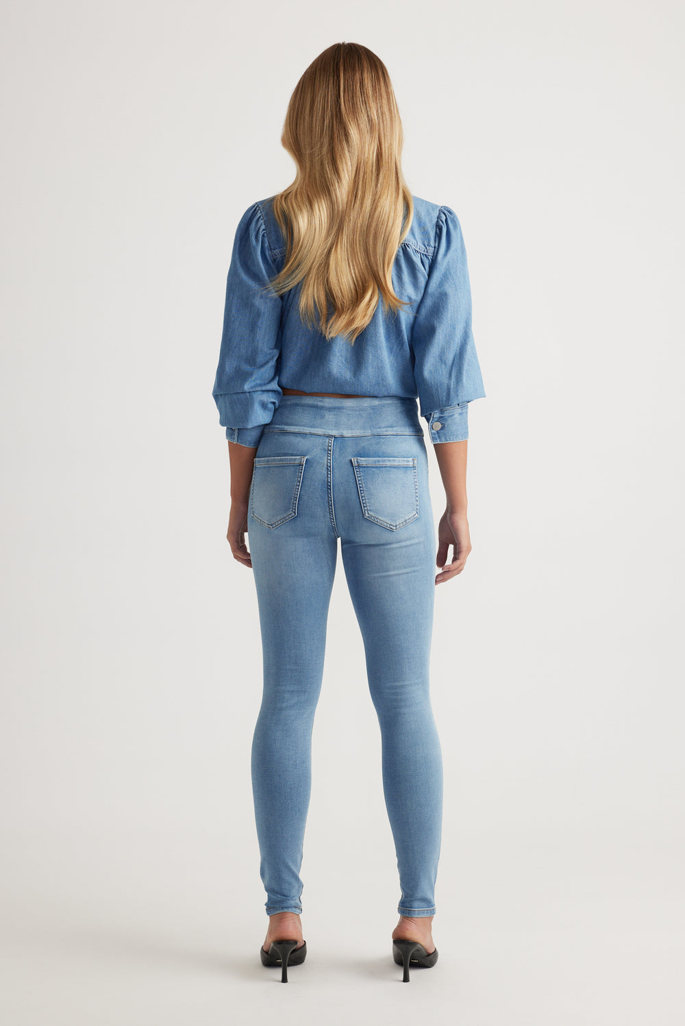 Rear view of model wearing light wash Riley Skinny Jean paired with denim top and black heels by Decjuba Australian brand