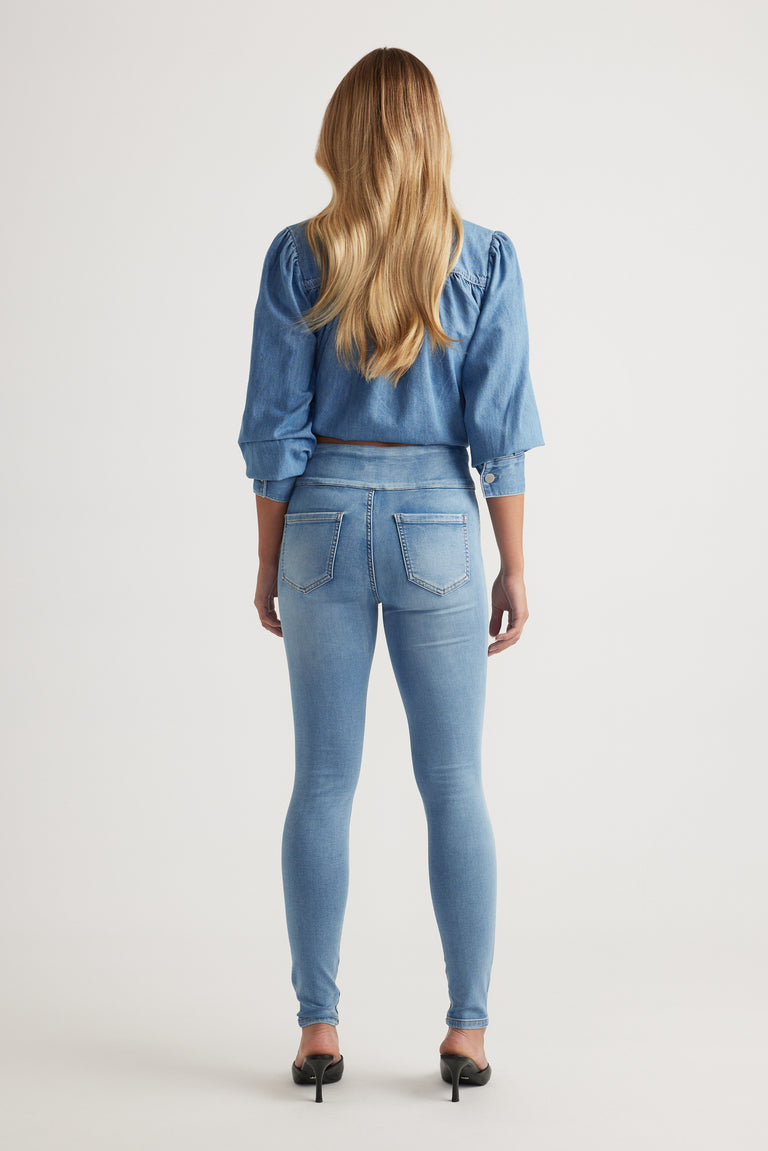 Rear view of model wearing light wash Riley Skinny Jean paired with denim top and black heels by Decjuba Australian brand