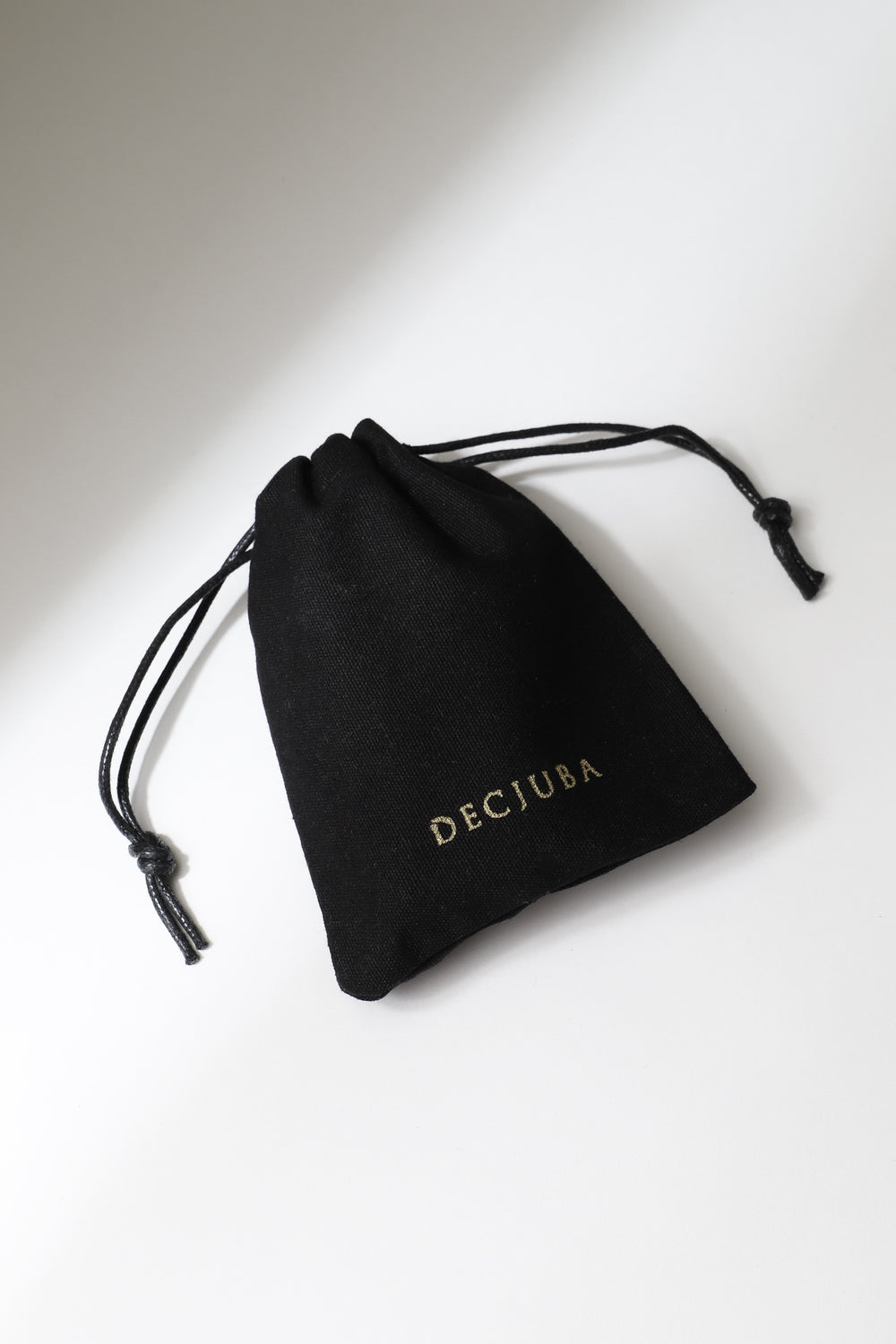 Small black drawstring pouch with gold branding, designed to protect delicate jewelry pieces.