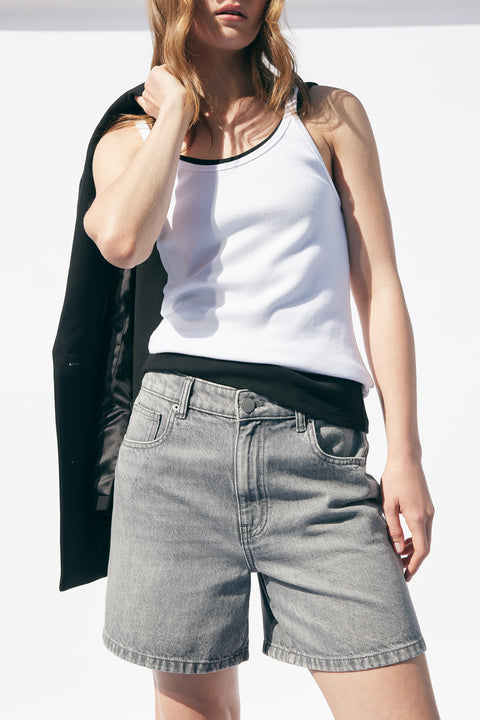 Woman wearing light gray denim shorts and a white ribbed tank top, black blazer casually draped over shoulder