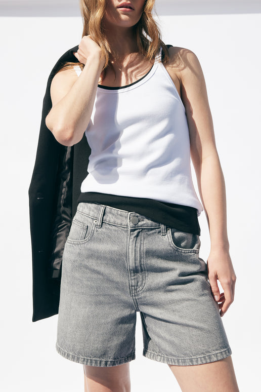 Woman wearing light gray denim shorts and a white ribbed tank top, black blazer casually draped over shoulder