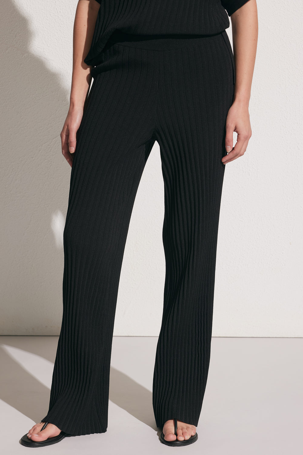 Close-up of a woman wearing black ribbed knit pants with a relaxed fit and straight leg, styled with a matching top