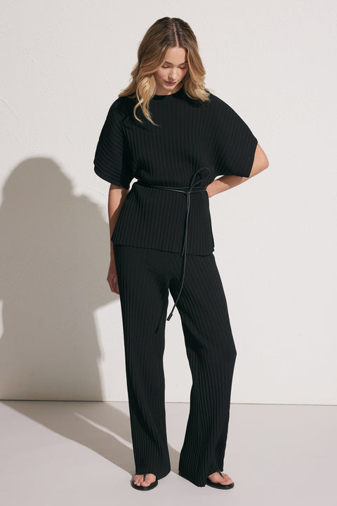 Woman wearing black ribbed knit top with wide sleeves and matching relaxed knit pants, styled with sandals