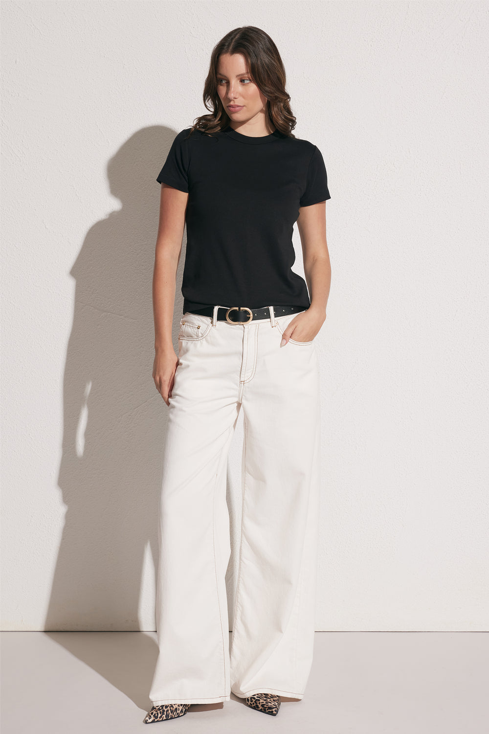 Woman wearing a fitted black crew neck tee paired with wide-leg white pants, black belt, and leopard print shoes, front view
