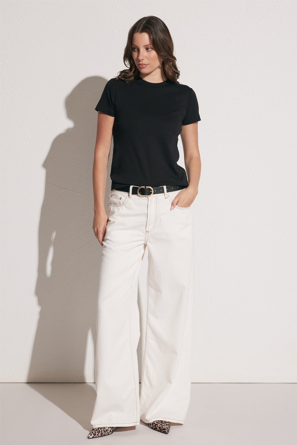 Woman wearing a fitted black crew neck tee paired with wide-leg white pants, black belt, and leopard print shoes, front view