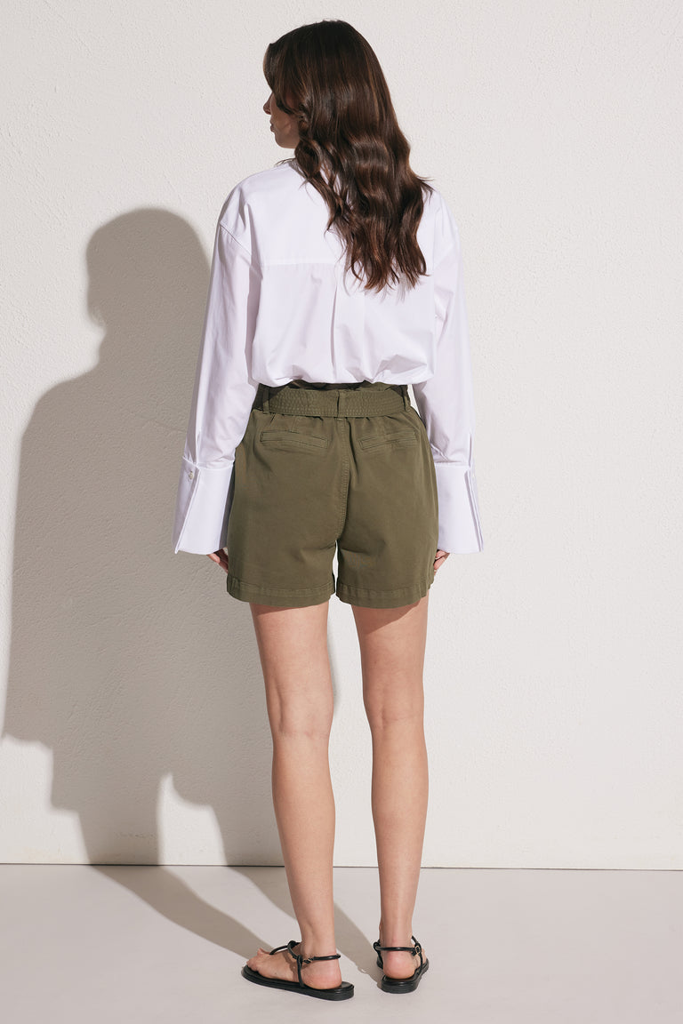 Woman wearing olive cargo shorts with an elastic waist and patch pockets styled with a white shirt and sandals