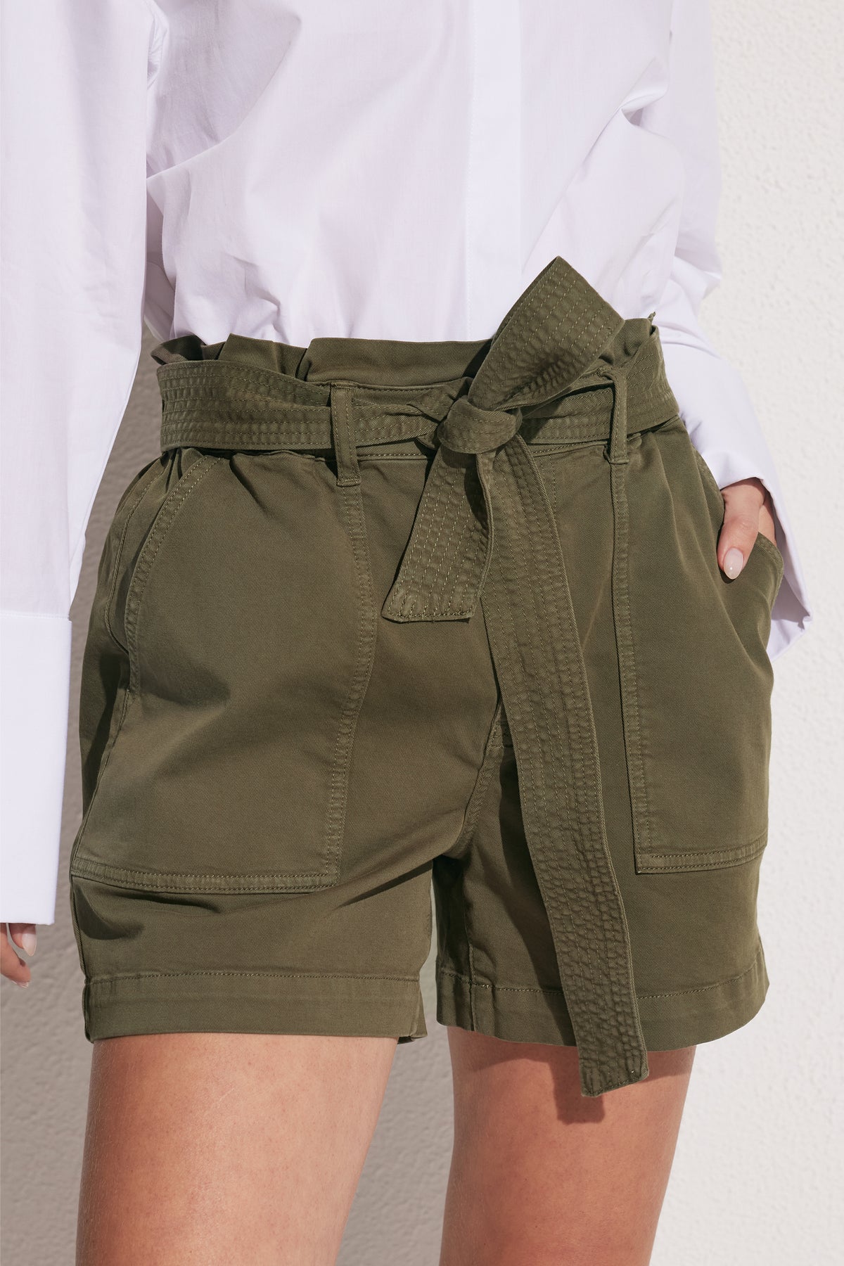 Woman wearing olive green high rise cargo shorts with a tie waist and functional patch pockets