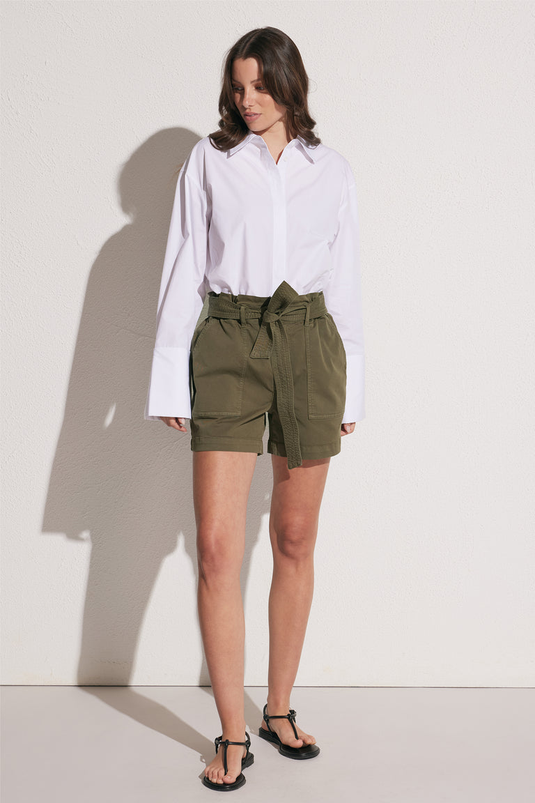 Woman wearing olive green high rise cargo shorts with a tie waist and patch pockets, styled with a white shirt and sandals