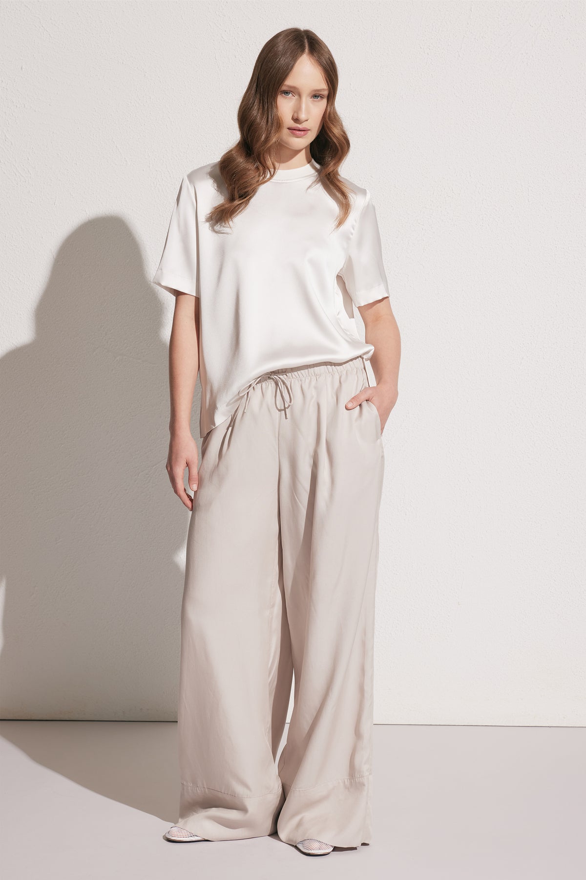 Front view of woman wearing loose beige wide-leg pants with drawstring waist paired with a short-sleeve satin tee