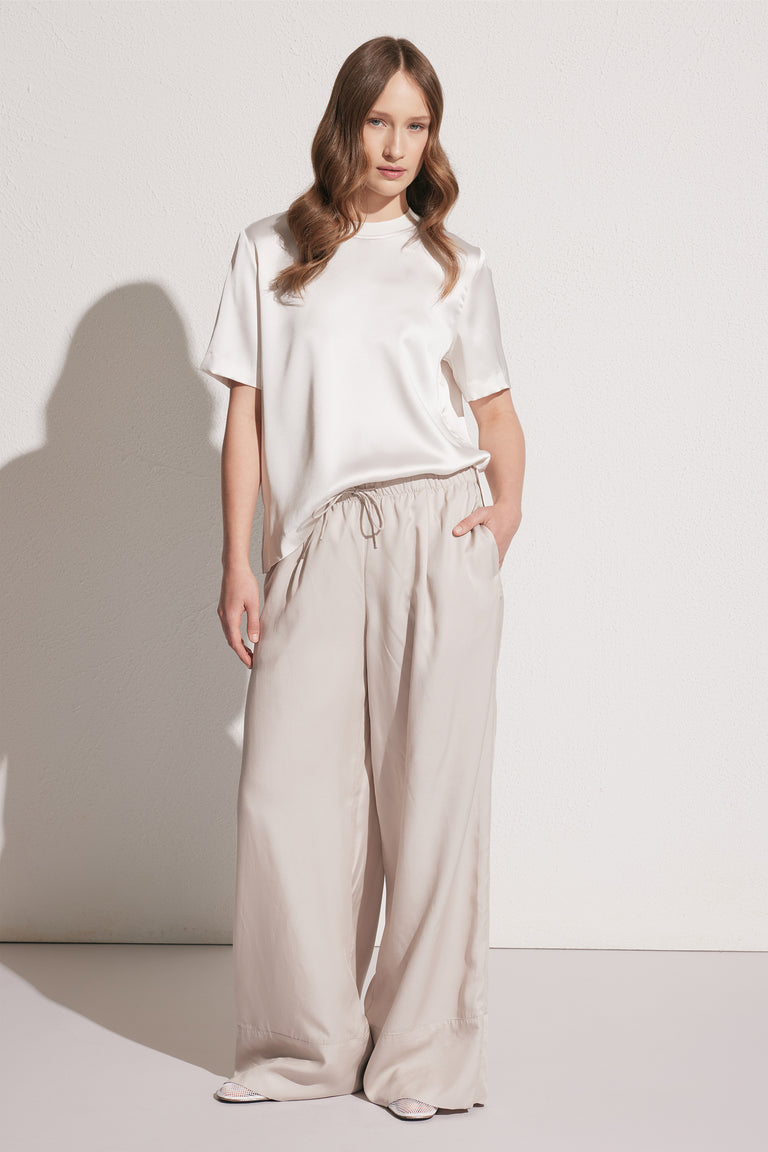 Front view of woman wearing loose beige wide-leg pants with drawstring waist paired with a short-sleeve satin tee