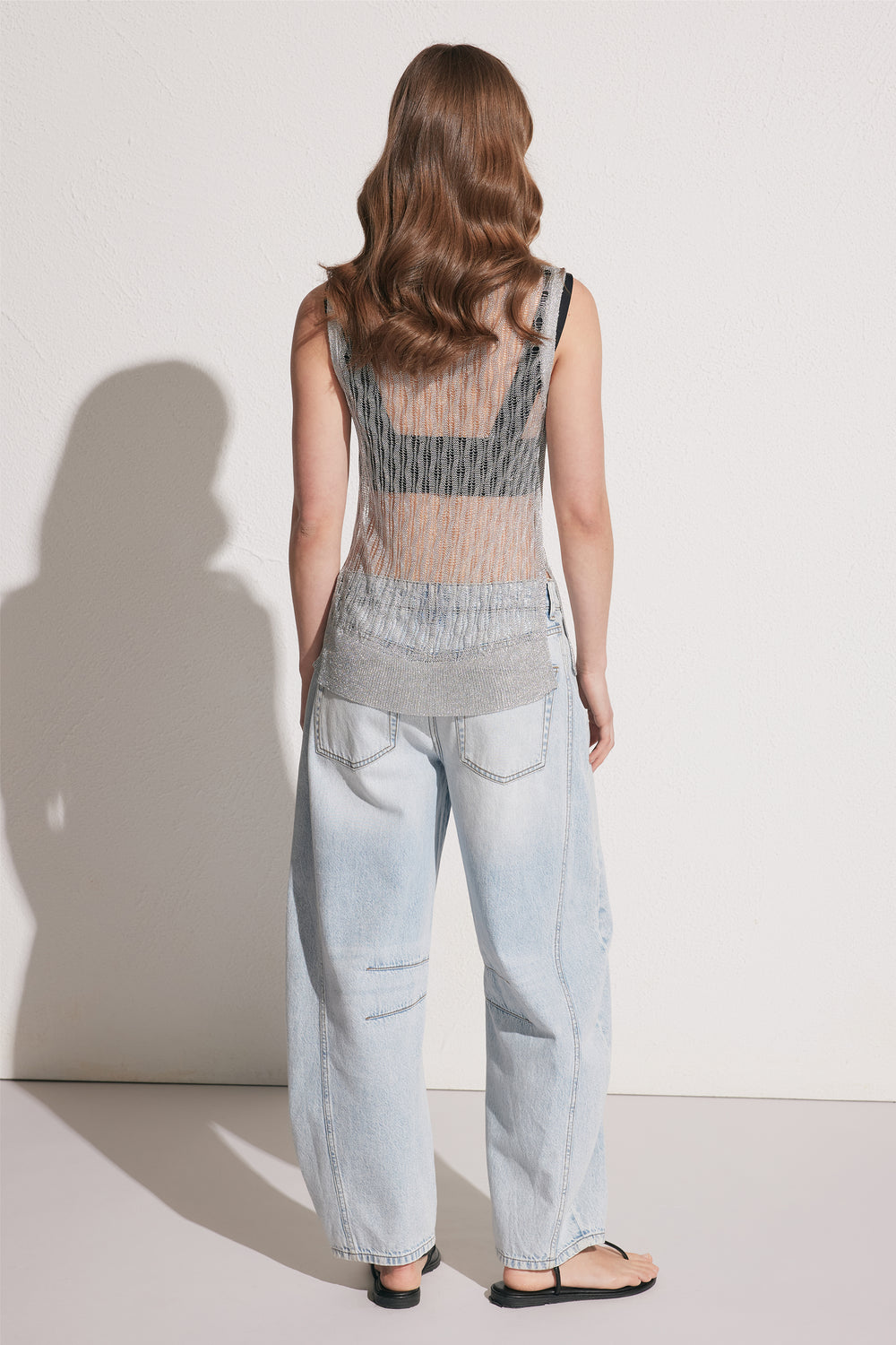 Back view of a woman wearing a metallic knit sleeveless tank with side splits and light wash jeans