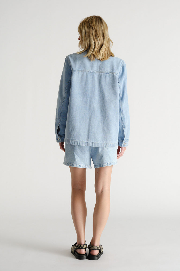 Woman seen from behind wearing a light blue denim jacket and matching D-Luxe shorts with black patterned sandals