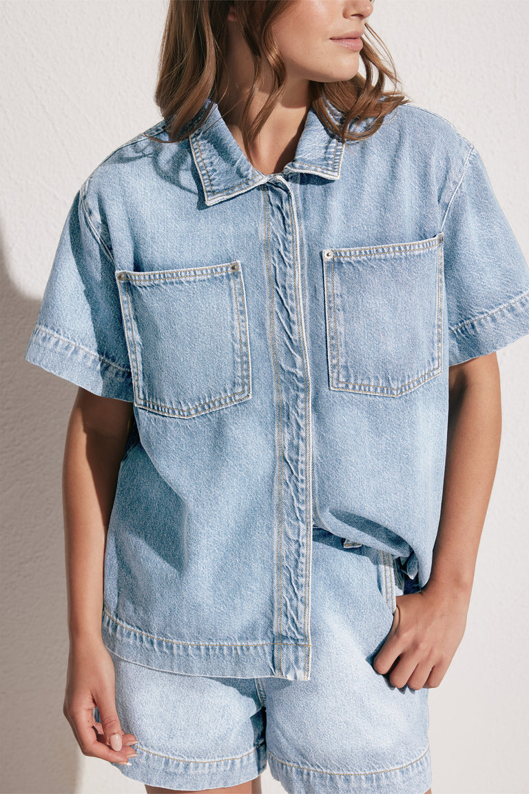 Woman wearing light blue high rise denim shorts with a matching short sleeve shirt and patch pockets