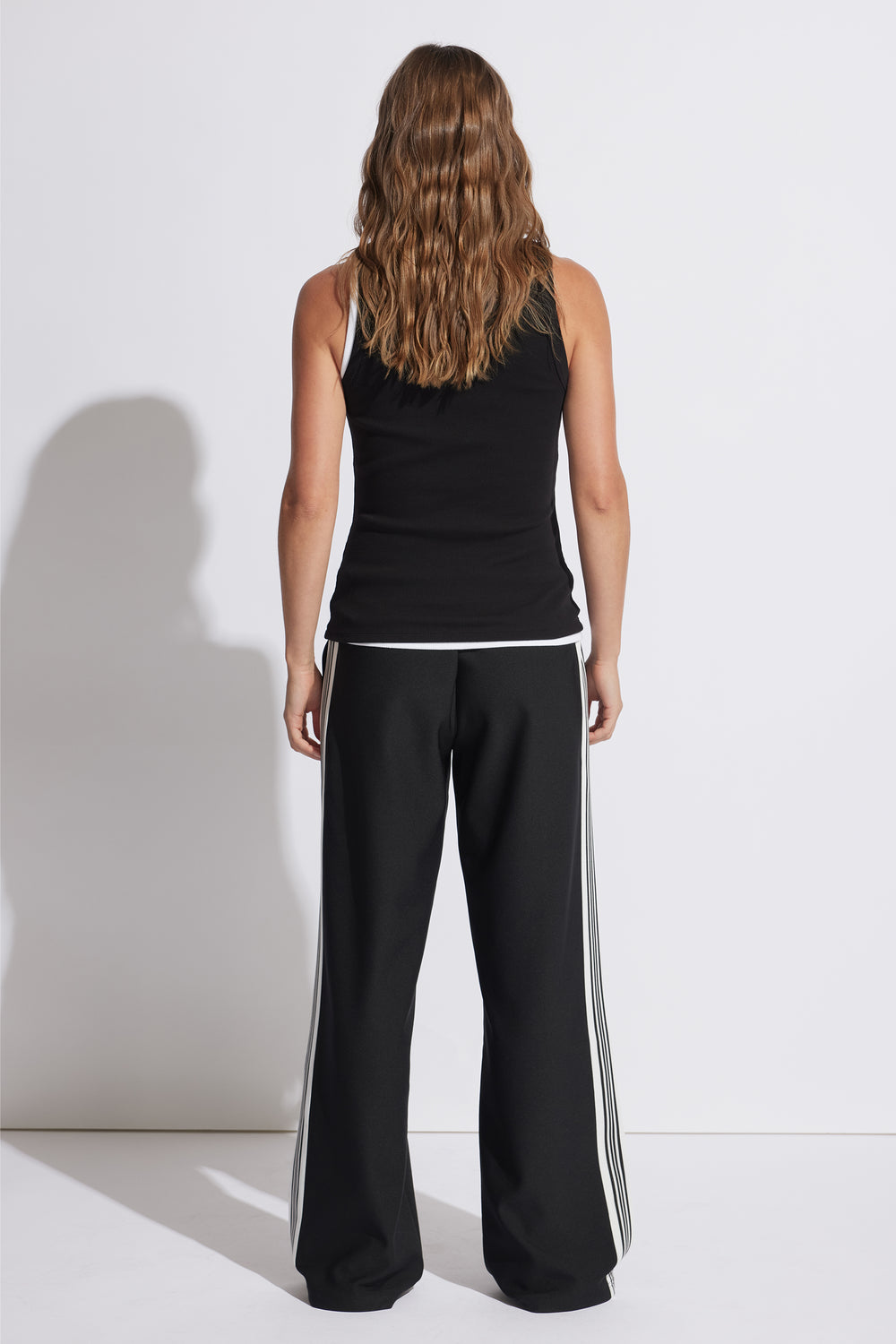 Woman wearing a fitted black ribbed tank top paired with wide-leg black pants featuring white side stripes.