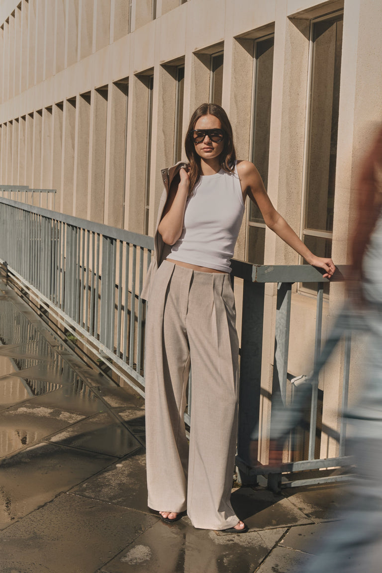 Woman wearing taupe pleated wide leg pants with a white tank top and sunglasses