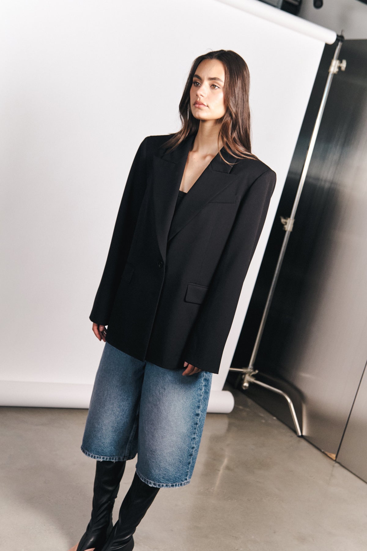 Woman wearing a black blazer with long blue denim shorts and knee high boots