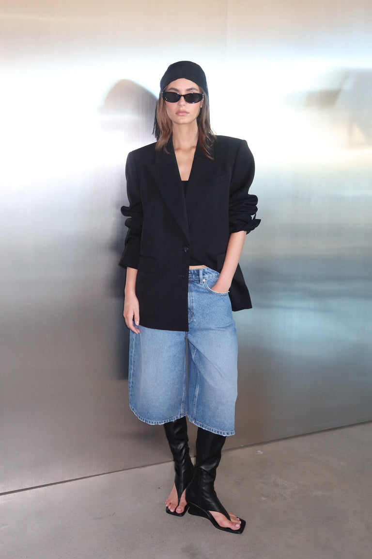Woman wearing an oversized black blazer with a blue denim midi skirt and sunglasses