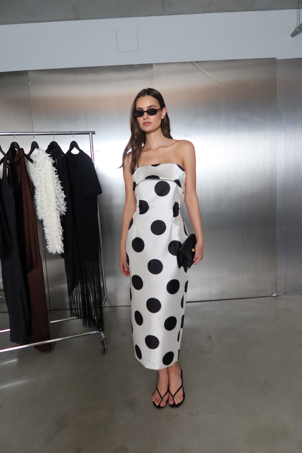 Woman wearing a strapless white and black polka dot fitted midi dress with sunglasses and sandals