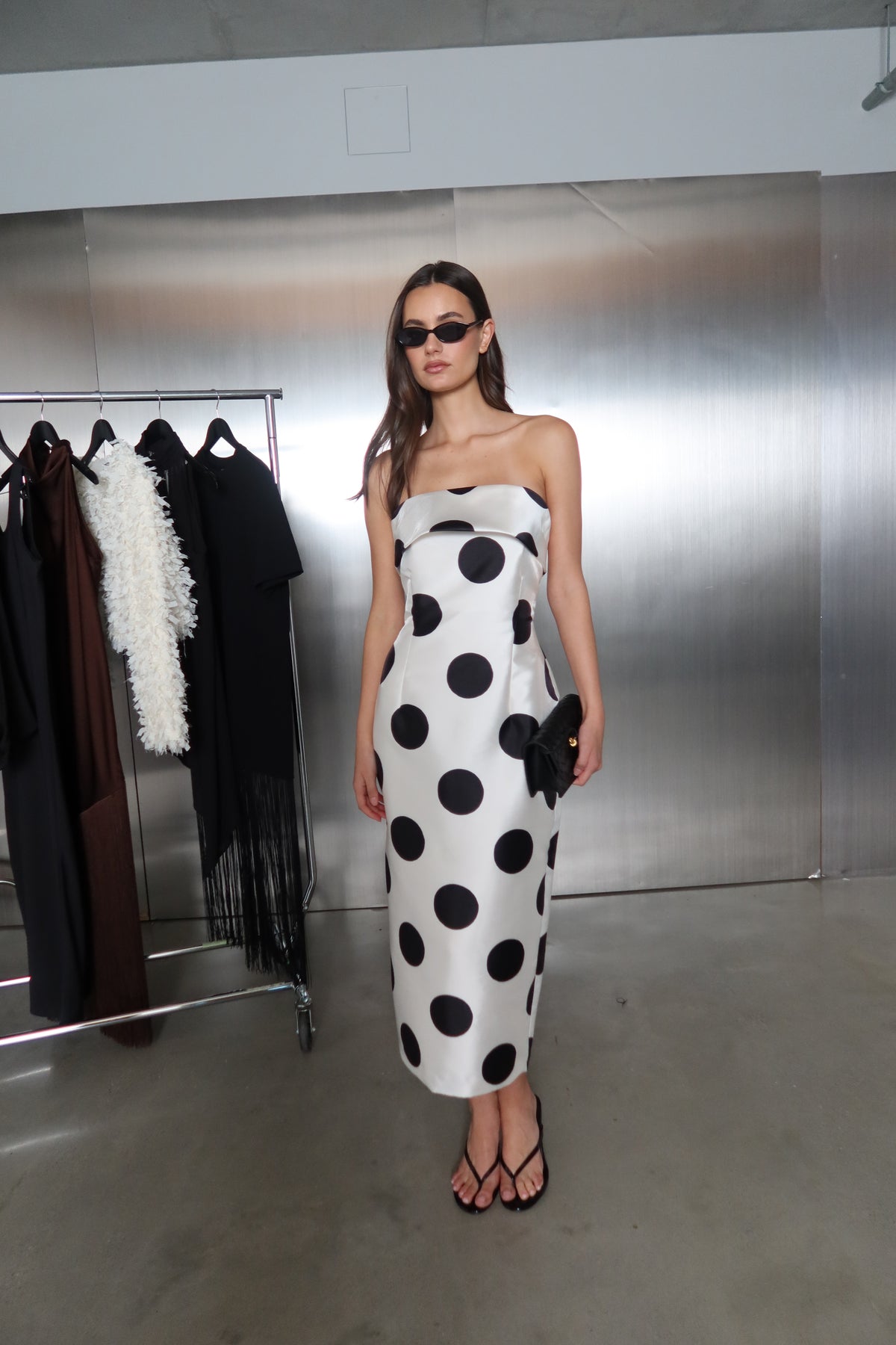 Woman wearing a strapless white and black polka dot fitted midi dress with sunglasses and sandals