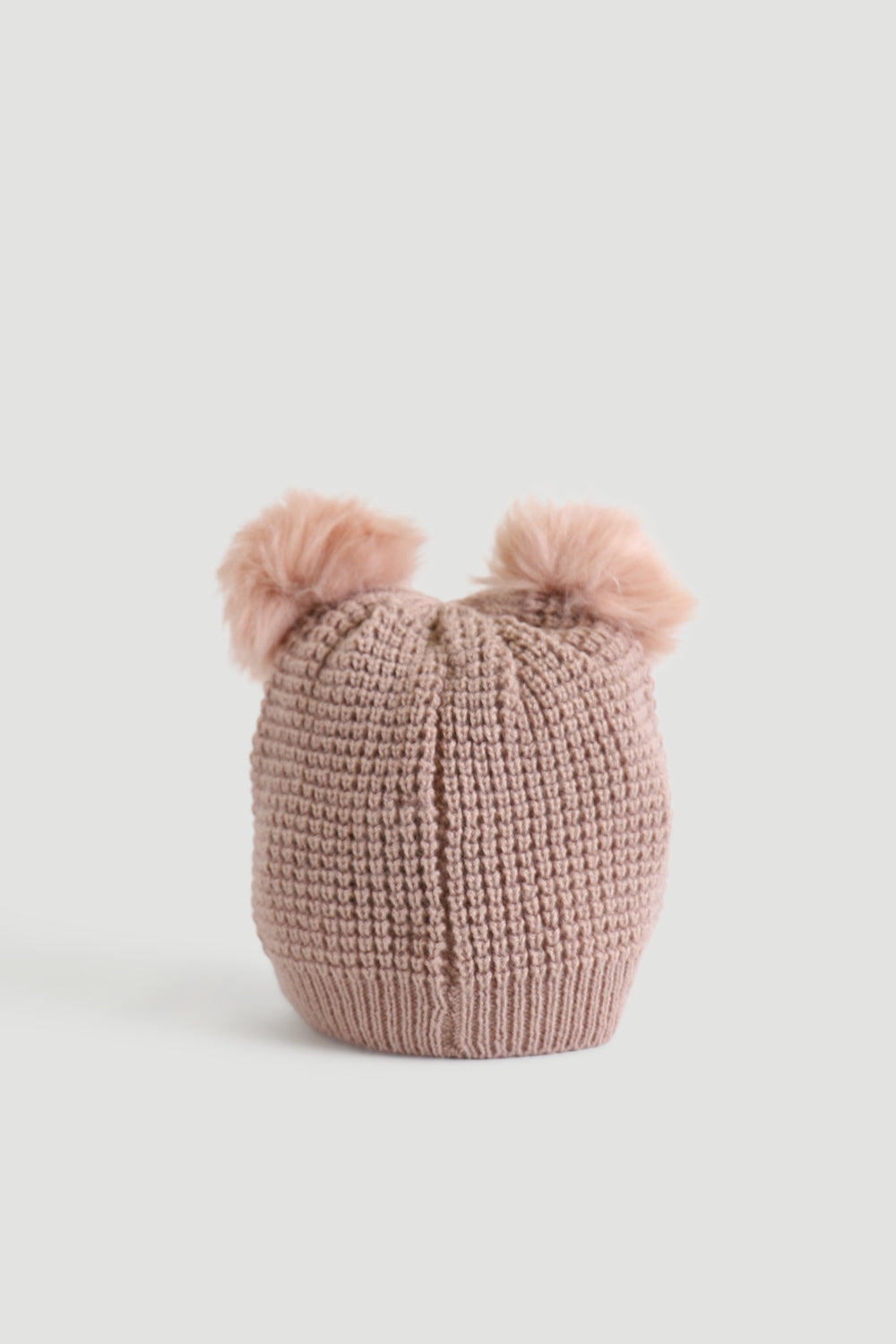 Soft pink knitted beanie with two fluffy pom-poms on top, displayed against a plain light background