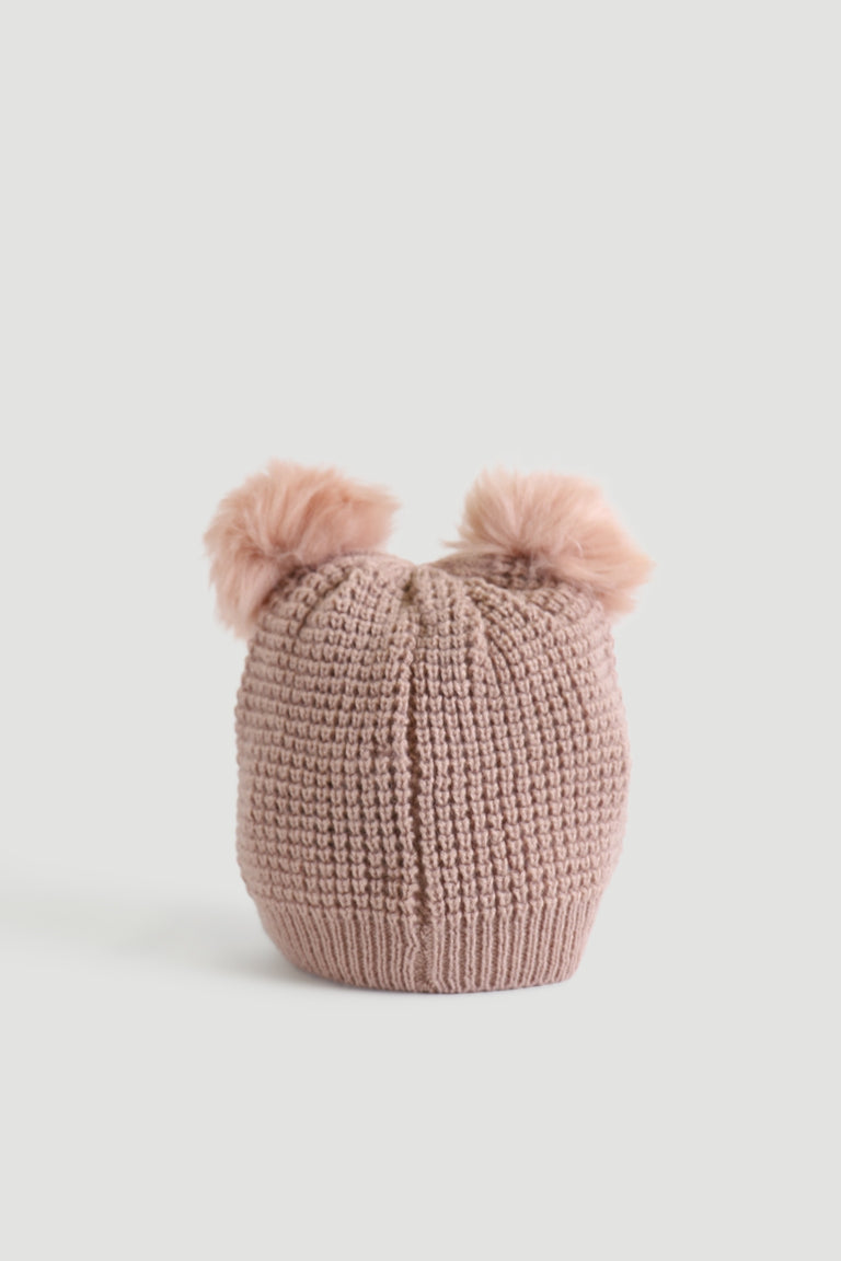 Soft pink knitted beanie with two fluffy pom-poms on top, displayed against a plain light background