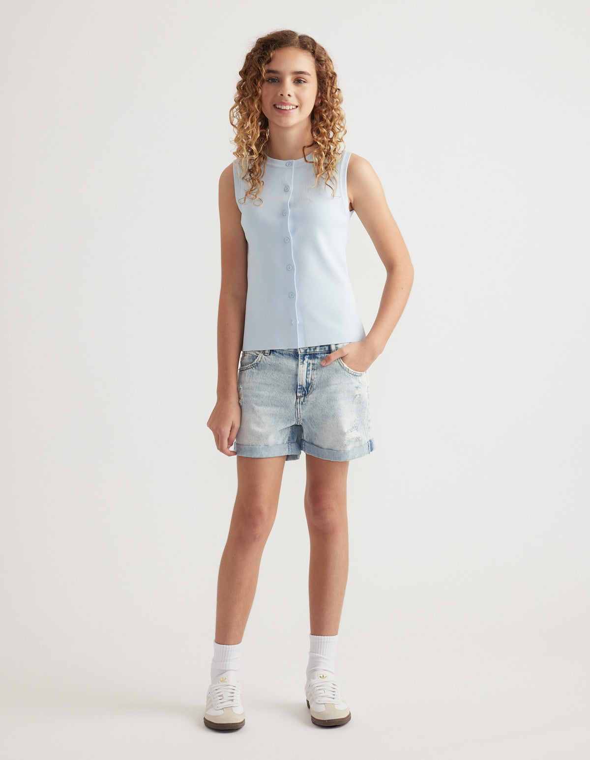 Girl wearing light wash distressed denim shorts with rolled cuffs, a sleeveless pale blue top and sneakers