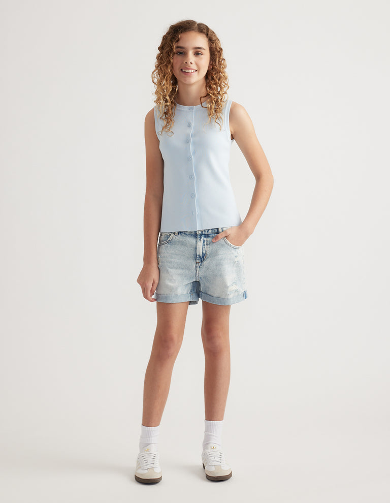 Girl wearing light wash distressed denim shorts with rolled cuffs, a sleeveless pale blue top and sneakers
