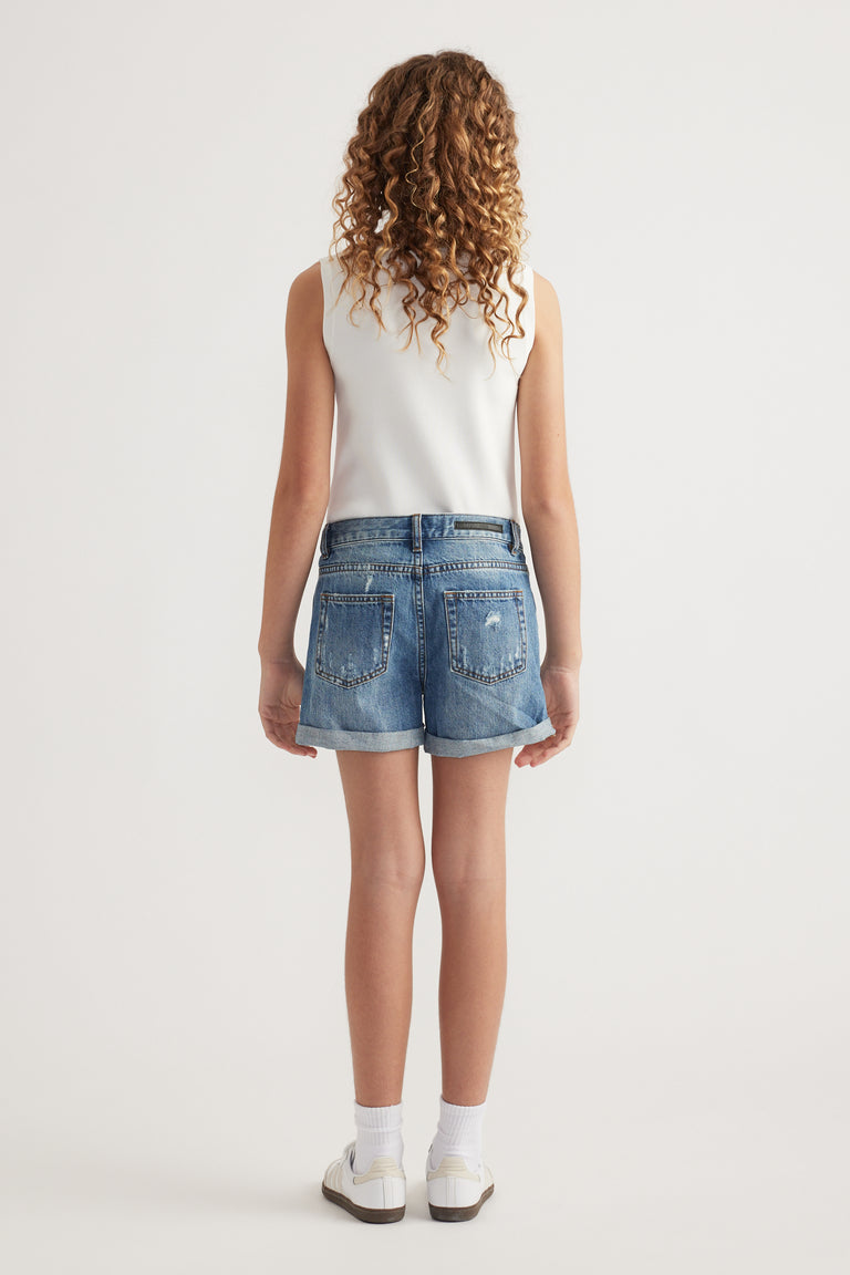 Back view of a girl wearing mid-rise blue denim shorts with distressed details and a cuffed hem
