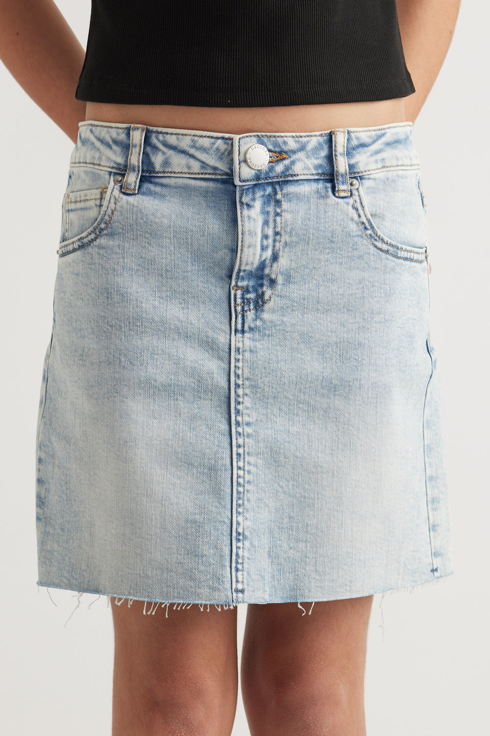 Front view of a light wash denim skirt with button and fly closure and raw frayed hem on a young model