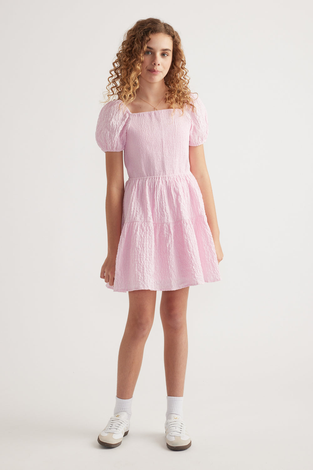 Girl wearing a pink textured mini dress with puff sleeves and white sneakers