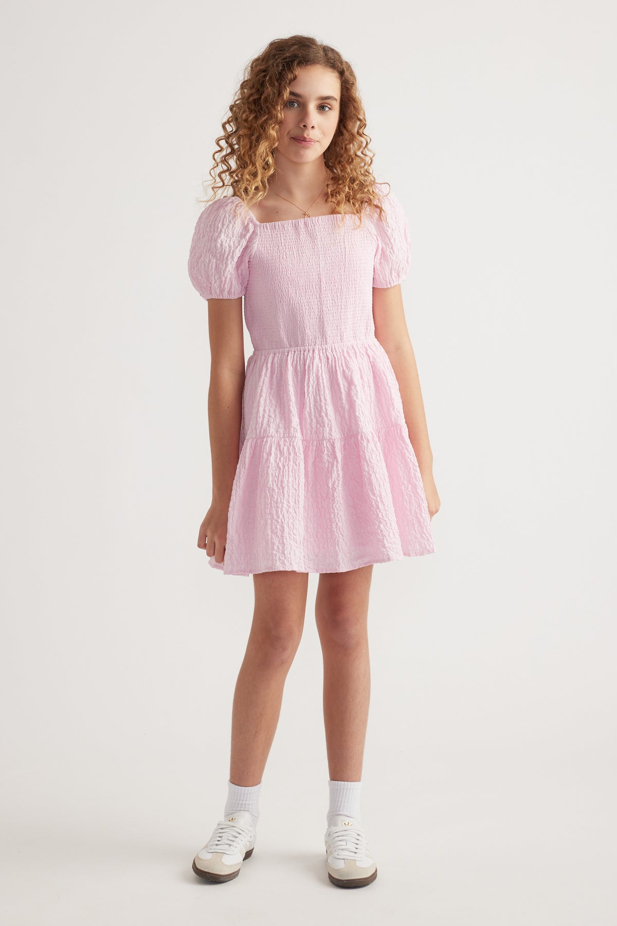 Girl wearing a pink textured mini dress with puff sleeves and white sneakers