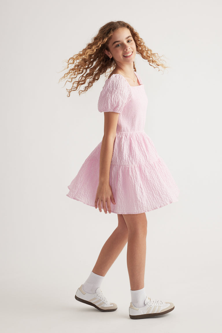 Girl wearing a pink textured mini dress with puff sleeves and white sneakers