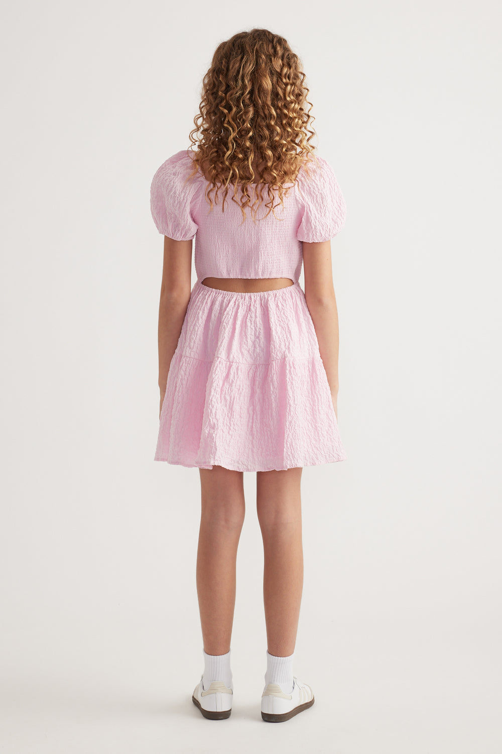 Girl seen from behind wearing a pink textured dress with puff sleeves and a back cutout