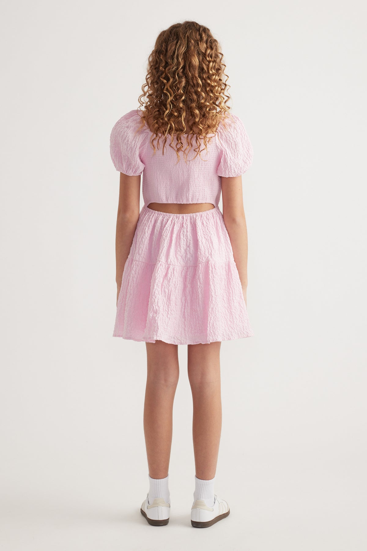 Girl seen from behind wearing a pink textured dress with puff sleeves and a back cutout
