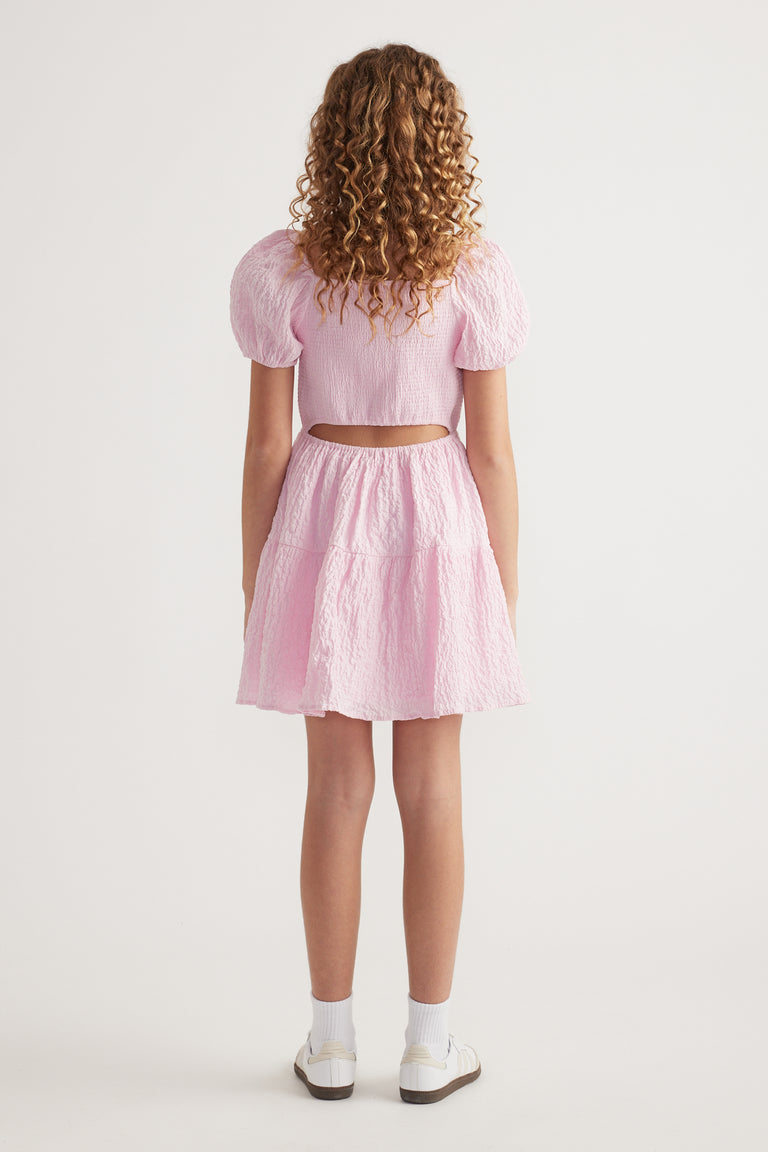 Girl seen from behind wearing a pink textured dress with puff sleeves and a back cutout