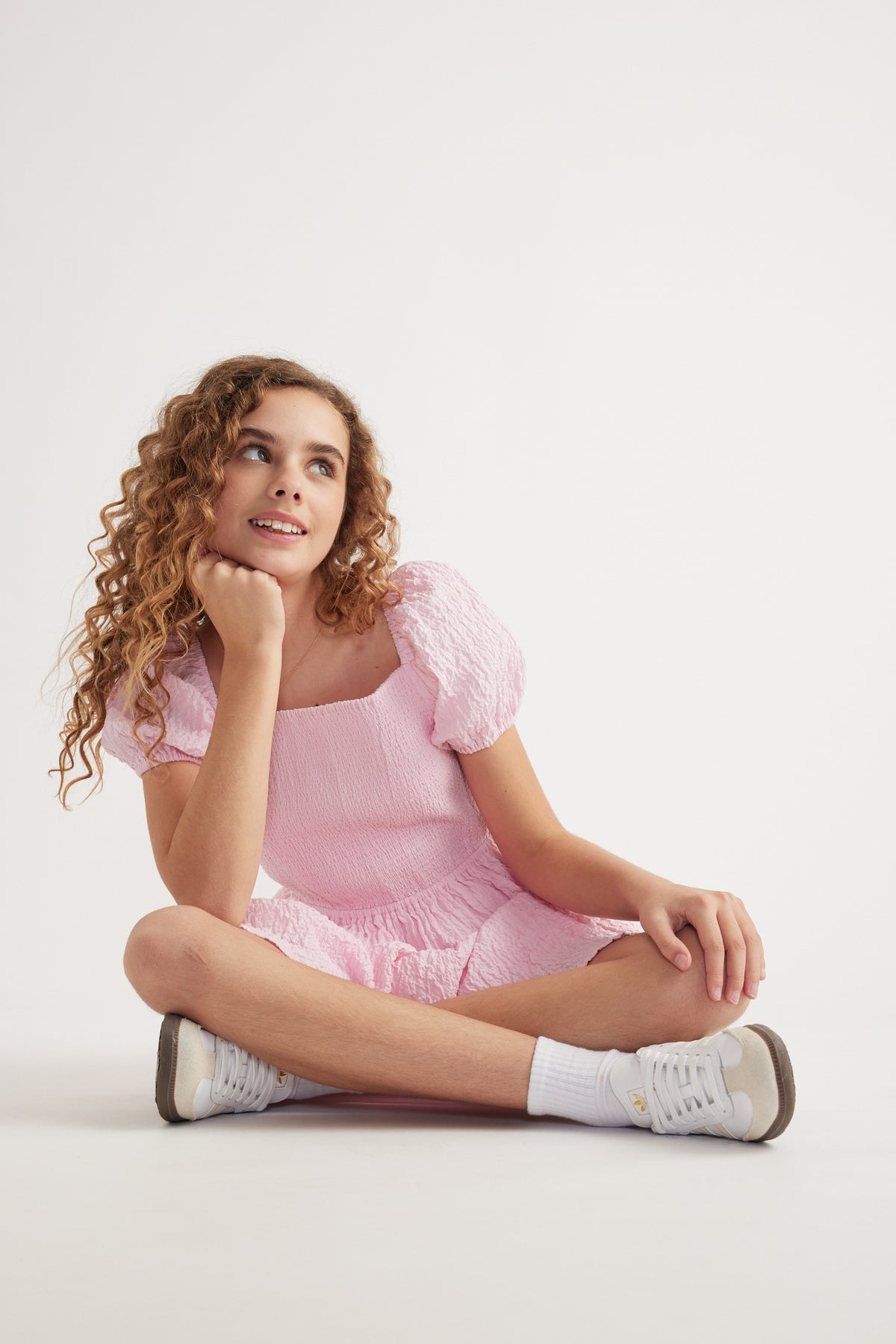 Girl wearing a pink textured mini dress with puff sleeves and white sneakers