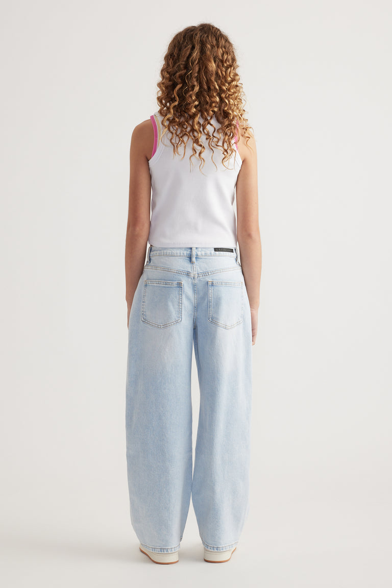 Rear view of girl wearing light wash baggy fit mid-rise jeans with a white sleeveless top against plain background