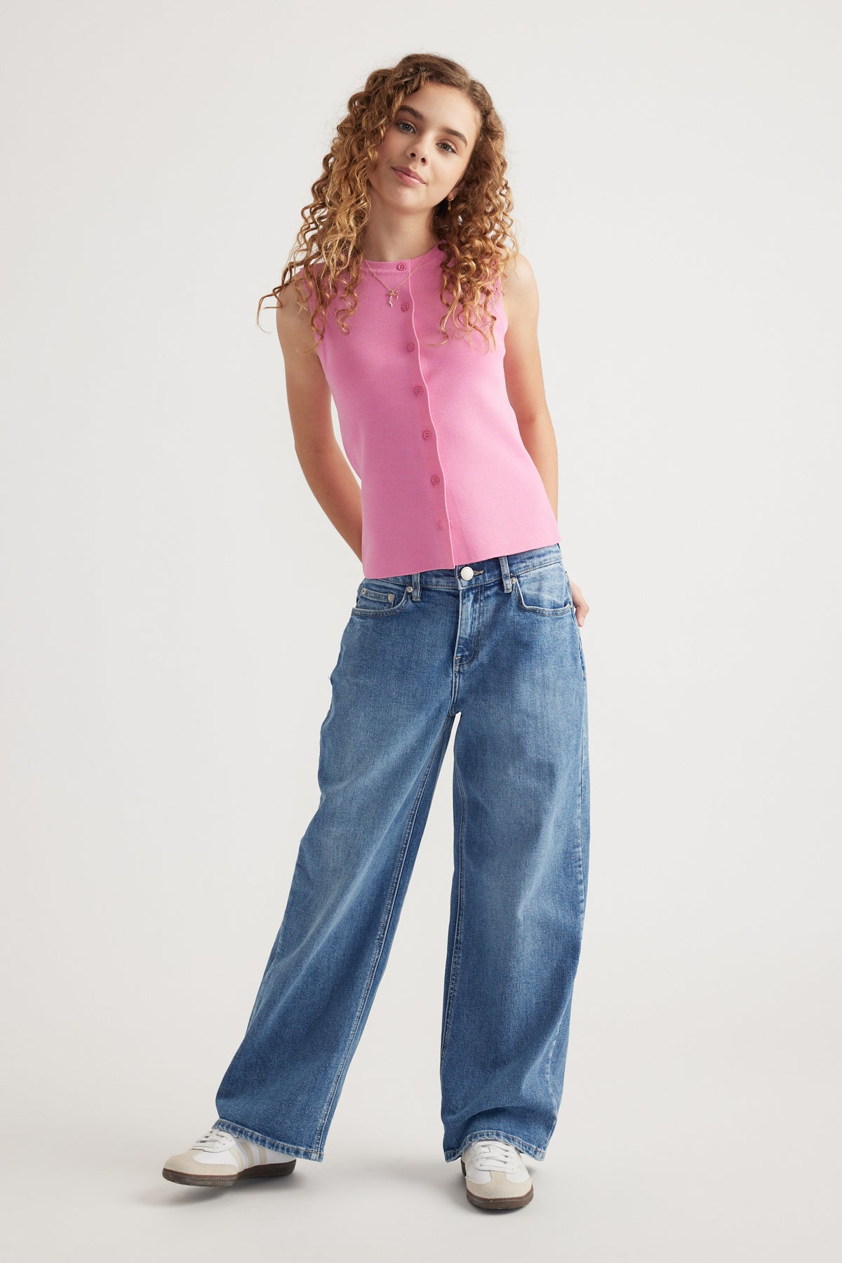 Girl wearing mid rise baggy fit blue jeans paired with a sleeveless pink button-front top and white sneakers