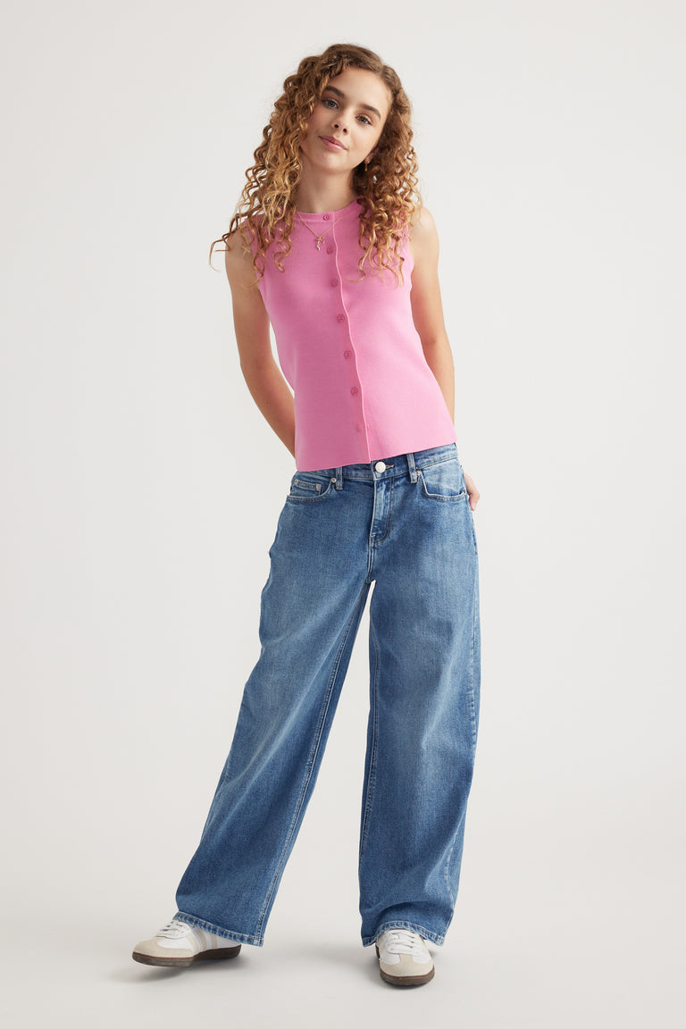 Girl wearing mid rise baggy fit blue jeans paired with a sleeveless pink button-front top and white sneakers