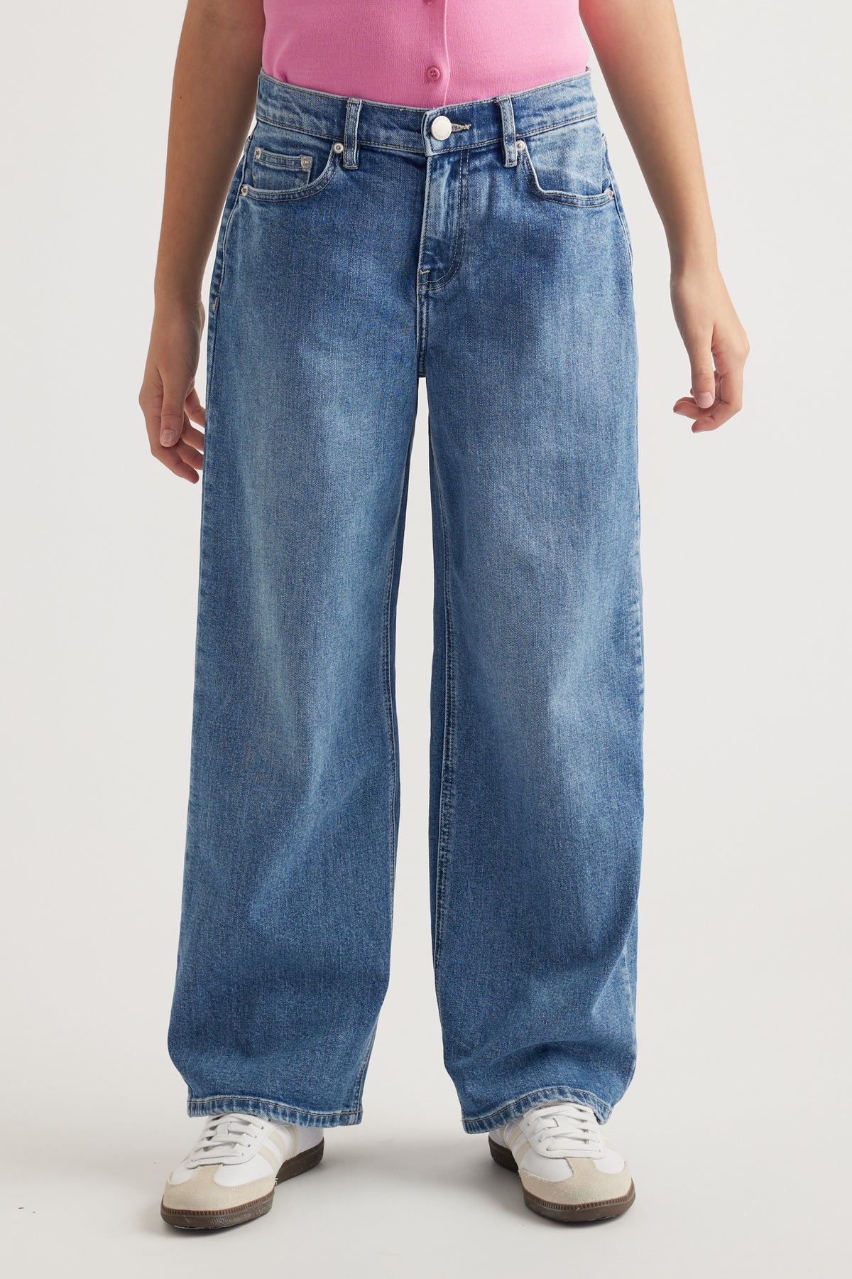 Front view of girl wearing mid-rise baggy fit blue denim jeans with functional pockets and white sneakers