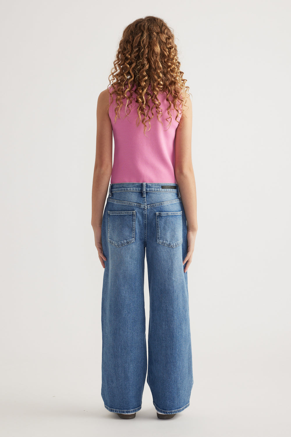 Rear view of girl wearing mid-rise wide-leg denim jeans paired with a sleeveless pink top
