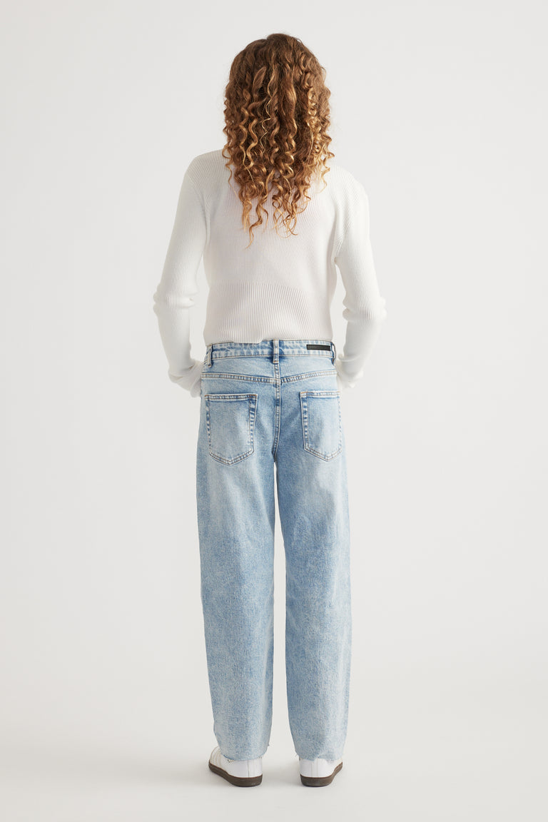 Rear view of girl wearing light wash straight leg jeans with raw hem paired with white long sleeve top