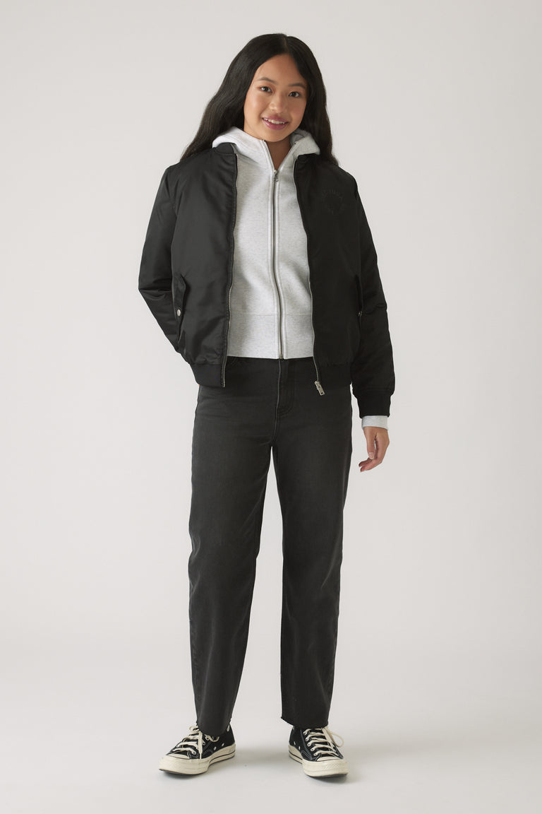 Girl wearing black straight leg jeans paired with a light zip-up hoodie and a black bomber jacket for casual style