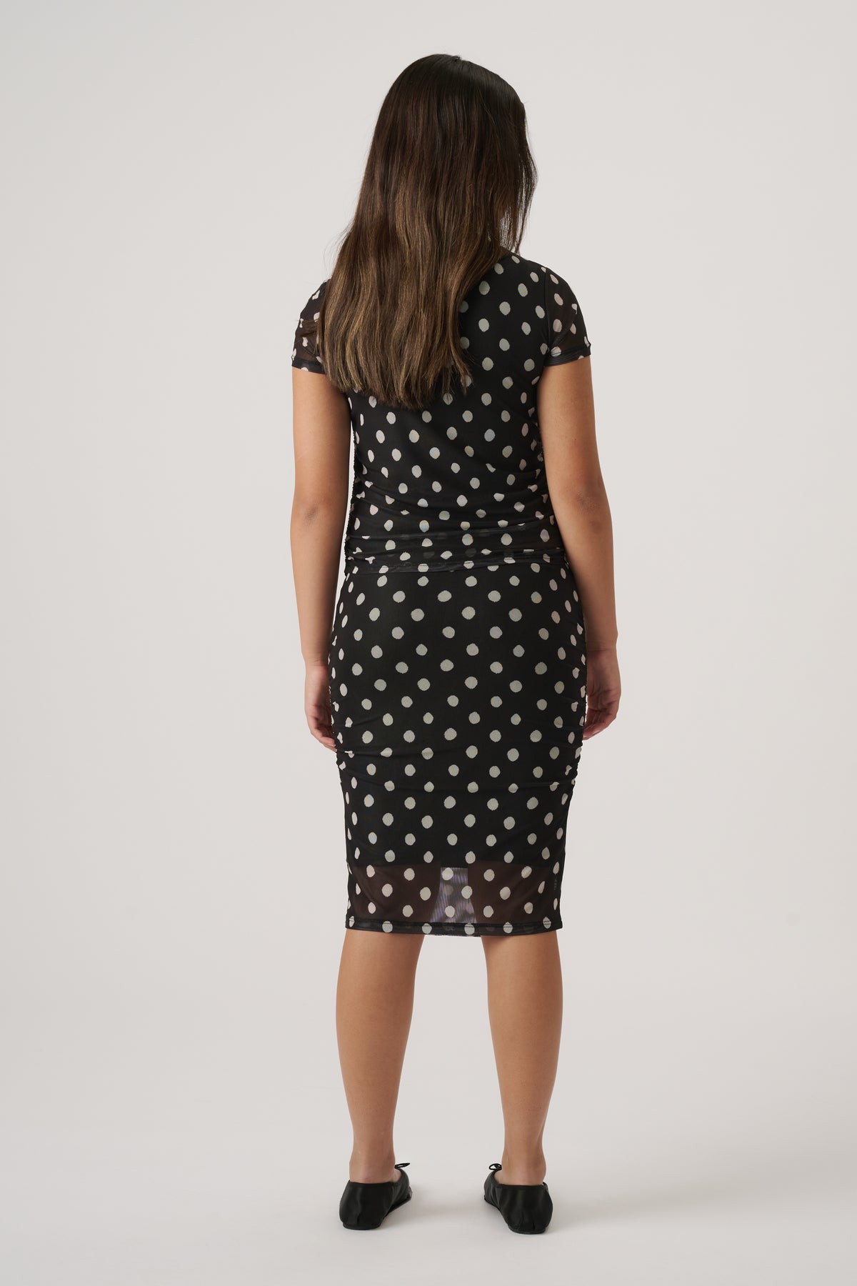 Girl wearing a fitted black mesh skirt with polka dots and a matching short-sleeve top, paired with black flats