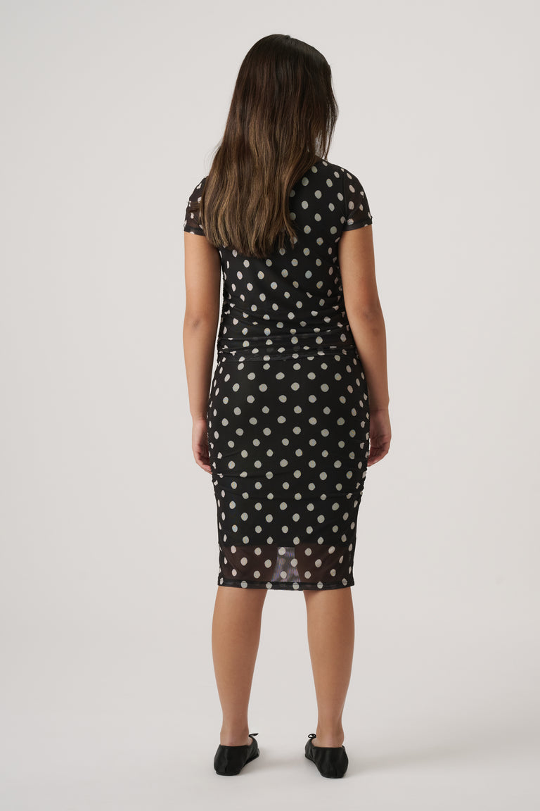 Girl wearing a fitted black mesh skirt with polka dots and a matching short-sleeve top, paired with black flats
